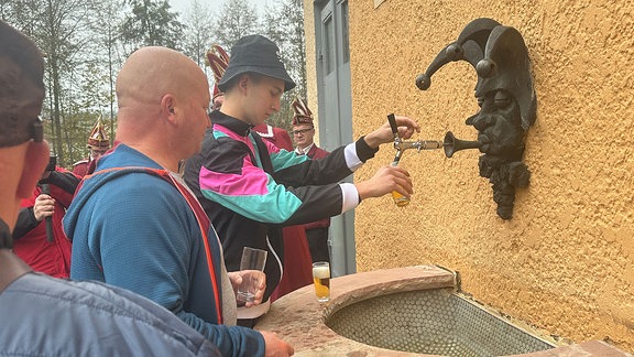 Männer zapfen Bier aus einem Hahn an einer Hauswand.