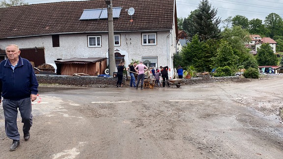 Menschen räumen nach Überflutung Schlamm von einer Straße.