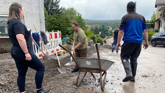 Menschen räumen nach Überflutung Schlamm von einer Straße.