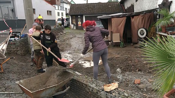 Menschen räumen nach Überflutung Schlamm von einem Grundstück