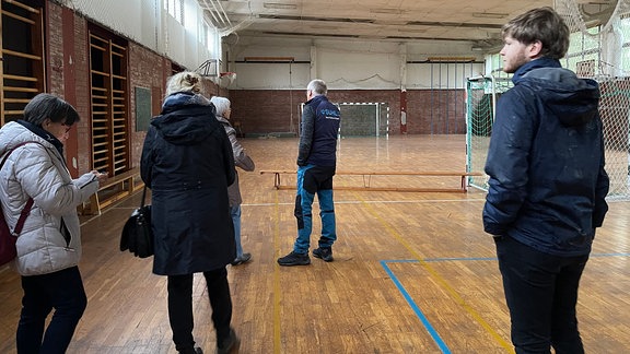 Menschen stehen in einer alten Turnhalle.