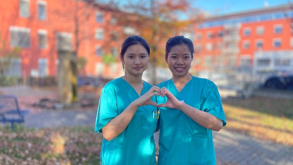 Trang (re.) und Huyen (li) stehen in ihrer türkisgrünen Krankenschwersterkleidung im Park hinter dem Marienstift Arnstadt  