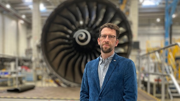 Ein Mann im blauen Kortanzug steht vor eine Flugzeugturbine. (Stefan Landes, Geschäftsführer von N3 in Arnstadt)