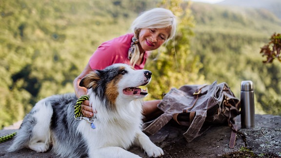 Eine ältere Frau sitzt auf einem Stein mit einem Hund