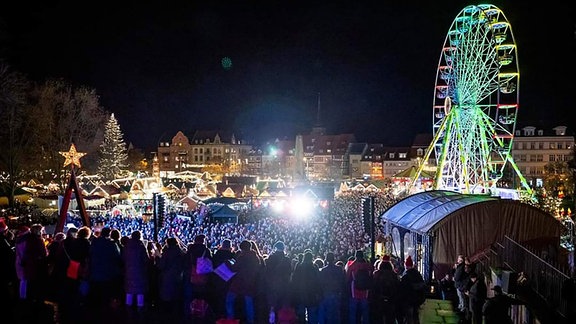 Blick von den Erfurter Domstufen auf den weihnachtlichen Domplatz mit Riesenrad und voller Menschen, die Weihnachtslieder singen