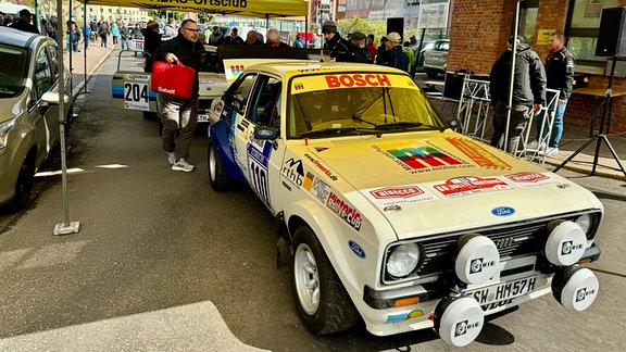 Technische Abnahme zur 60. Rallye Wartburg Eisenach: Menschen an einem Renn-PKW unter einem gelben Zeltdach