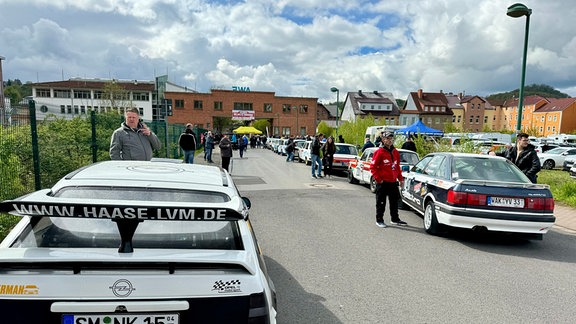 Technische Abnahme zur 60. Rallye Wartburg Eisenach. Blick in eine Straße: Menschegruppen neben ihren Autos bei der Rennvorbereitung