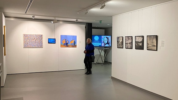 Blick in einen Ausstellungsraum mit Wänden, an denen Kunstwerke hängen.