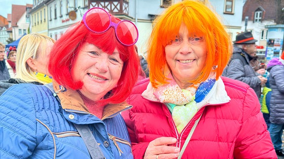 Karneval Bad Salzungen: Zwei Frauen mit roter und oranger Perücke und Verkleidungs-Brille in Winterkleidung posieren mit Sekt in der Hand