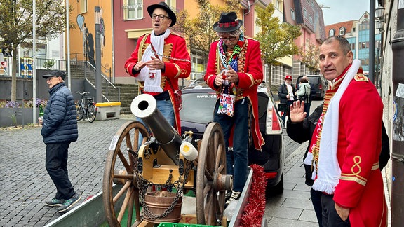 Karneval Bad Salzungen: Mehrere Männer sind in roten Roben verkleidet, zwei stehen auf einem Anhänger mit Kanone und Bierkasten