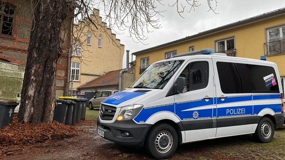 Während einer Razzia steht ein Polizeiwagen vor einem Haus