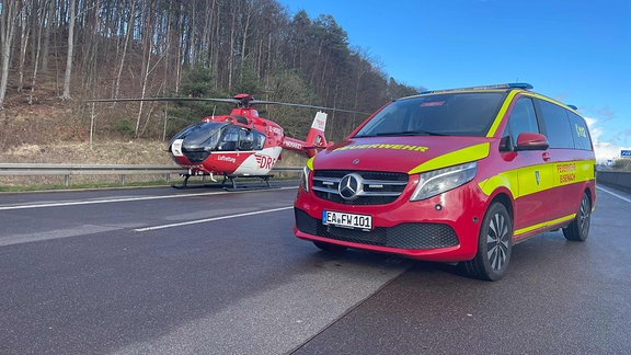 Ein Rettungshubschrauber steht neben einem Auto der Feuerwehr auf einer Autobahn