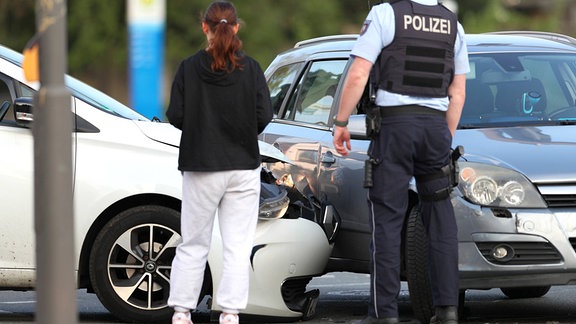 Zwei Autos stehen nach einem Unfall an der Unfallstelle Kreuzung. Ein Polizist betrachtet den Schaden.