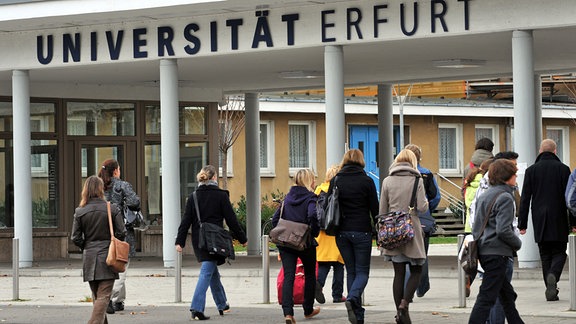 Studenten gehen durch den Eingang der Universität in Erfurt. 