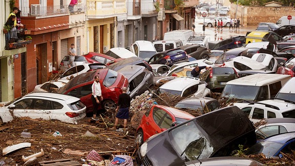 Anwohner einer Straße in Valencia betrachten durch Wassermassen aufgestapelte Autos