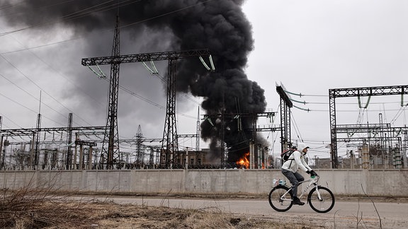 Ein Mann radelt nach einem russischen Angriff an einem Elektrizitätswerk vorbei.