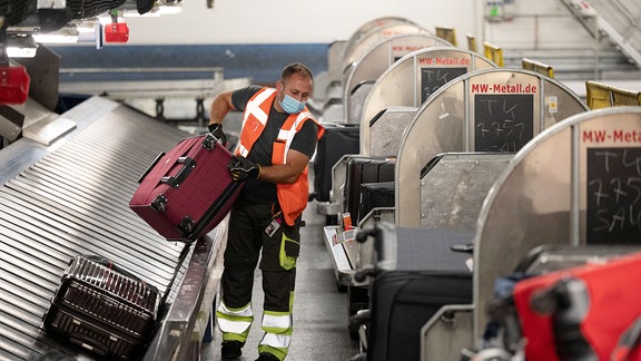 Ein Arbeiter hebt im Gepäckverteiler des Flughafen Stuttgart einen Koffer von einem Gepäckband auf einen Gepäcktransportwagen.