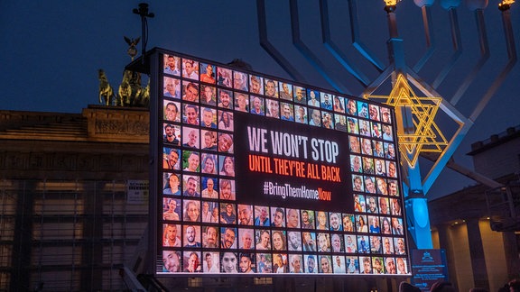 Auf einem Displayboard sind die Geiseln abgebildet, die am 7. Oktober 2023 von der Hamas aus Israel entführt wurden, während das Chanukka-Festes mit dem Anzünden des ersten Lichtes an einem großen Chanukka-Leuchter in Anwesenheit des Bundeskanzlers am Brandenburger Tor in Berlin eröffnet wird.