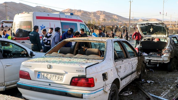 Menschen stehen neben zerstörten Autos nach einer Explosion. 