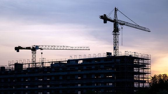 Kräne stehen hinter dem Rohbau für ein Bürogebäude auf einer Baustelle am Airport Leipzig/Halle in Schkeuditz.