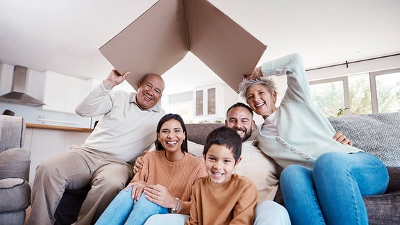 Symbolbild Bausparen - Eine Familie hält ein Dach aus Pappe über ihre Köpfe