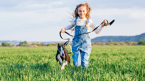 ein Mädchen läuft mit ihrem Hund über eine Wiese