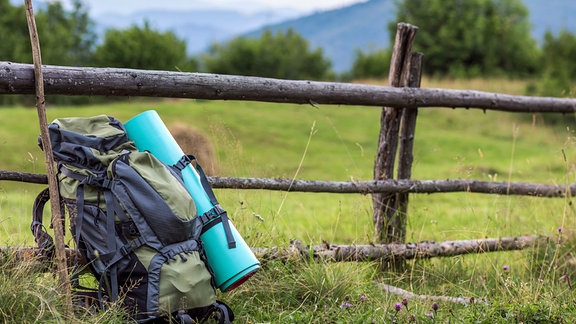 Ein Trekkingrucksack lehnt an einem Zaun, daneben steht ein Wanderstock.