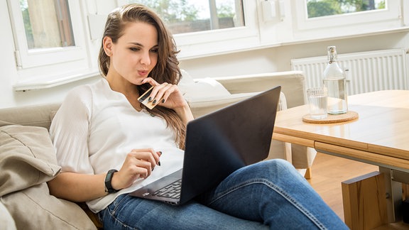 Eine Frau haelt eine Kreditkarte in der Hand und schaut auf einen Laptop