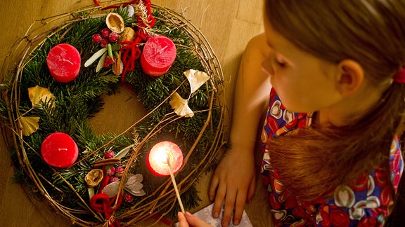 Kind zündet Kerze auf einem Adventskranz an