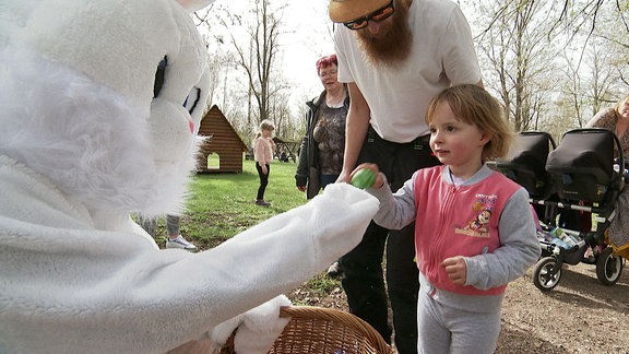 Ein Kleinkind bekommt vom Osterhasen ein Osterei überreicht.