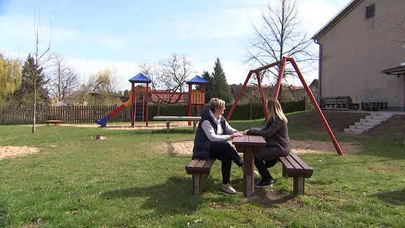 Zwei Frauen sitzen an einem Tisch bei einem Spielplatz.