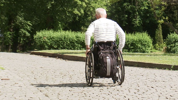 Ein Rollstuhlfahrer fährt auf einer Pflastersteinstraße.