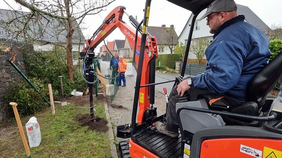 Bagger mit Bohraufsatz bohrt ein Loch in den Erdboden.