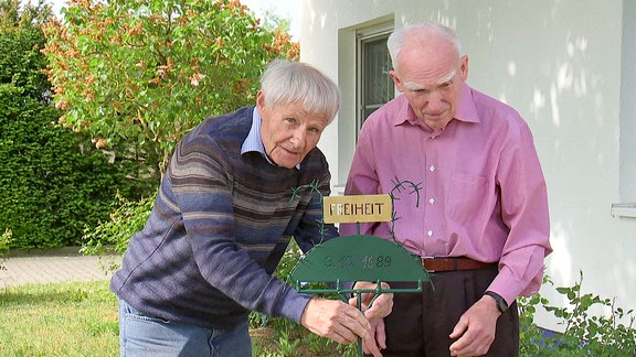 Zwei Männer stecken ein Gartenschild in den Boden