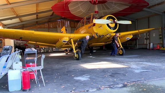 Zwei Männer schieben eine Maschine aus dem Hangar