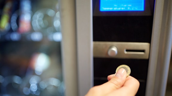 Eine Hand mit Münze an einem Lebensmittelautomat