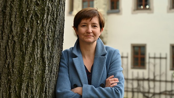 Eine Frau in blauer Jacke lehnt an einem Baum