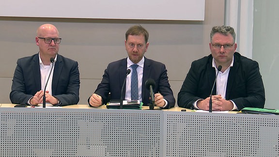 Michael Kretschmer sitzt während einer Pressekonferenz zwischen zwei Kollegen.