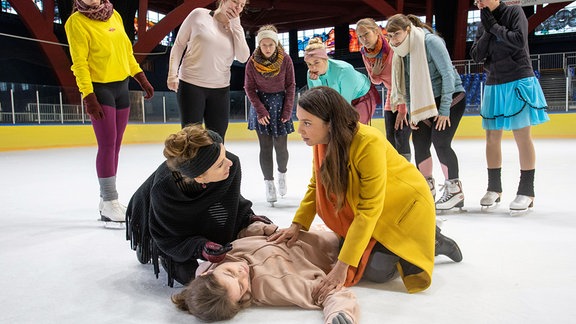 Solveig Dietze (Linda Stockfleth, liegend) liegt auf dem Eis.. . Ihre Mutter Jutta (Judith Rosmair, li.) und Arzu Ritter (Arzu Bazman, re.), die gerade mit ihren Söhnen zu einer Schnupperstunde vorbeischaut, beugen sich über sie.