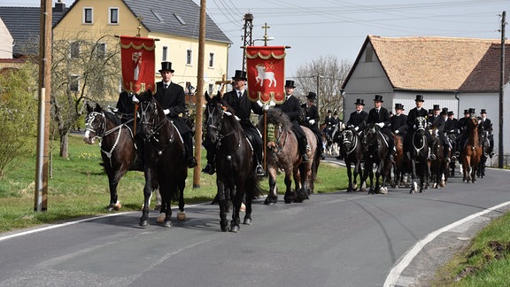 Männer mit Zylindern reiten auf geschmückten Pferden.