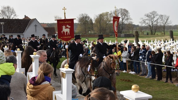 Männer mit Zylindern reiten auf geschmückten Pferden.