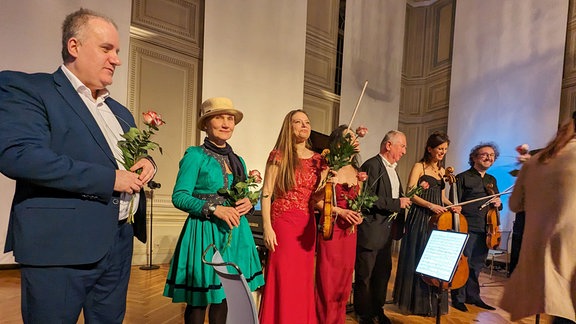 Musiker*innen stehen in einer Reihe und halten Rosen in den Händen.