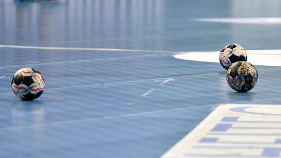 Drei Bälle liegen auf einem Handballfeld.