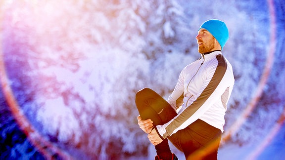 Ein junger Mann im Sportdress macht Gymnastik im Schnee.