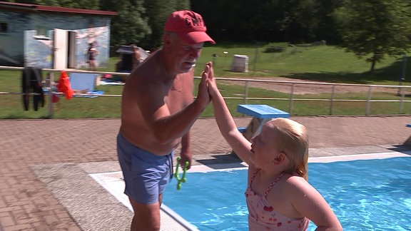 Schwimmlehrer und Schwimmschülerin klatschen sich am Beckenrand ab