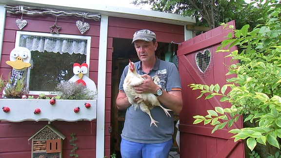 Ein Mann hält im Garten Paradies der Sinne ein Huhn in der Hand