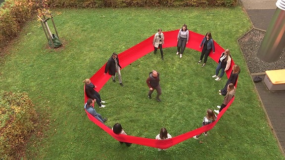 Menschen stehen im Kreis mit einem roten Band im Rücken