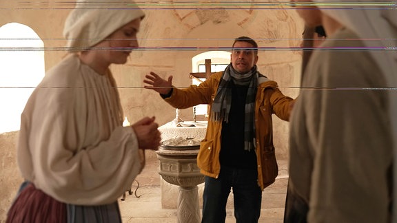 Eine Frau in historischem Kostüm in einer Kirche bekommt Regieanweisungen von einem Mann