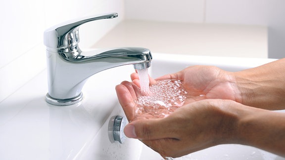 Hände unter einem aus einem Wasserhahn sprudelnden Wasserstrahl