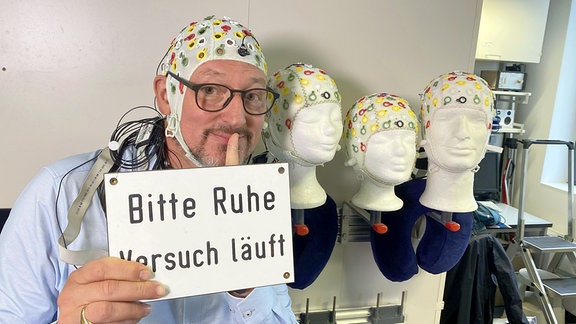 Ein Mann hält ein Schild: "Bitte Ruhe -- Versuch läuft."